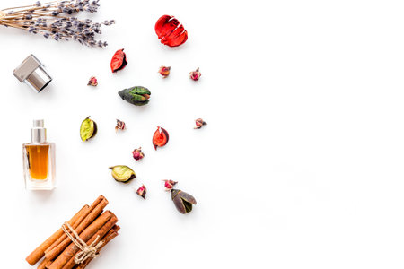 Bottle of perfume near dry flowers, cinnamon and candles on white background top view.