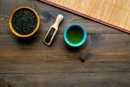Chinese tea concept. Dry tea leaves in bowl and wooden scoop near cup of tea on rustic wooden background and bamboo table mat top view.の写真素材