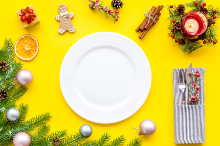 Christmas and new year decoration with gift box, plate and fir tree on yellow table background top view space for textの写真素材