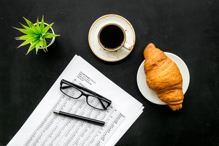 Pencil, glasses, documents, cup of coffee and croissant for business lunch in office on black background top viewの写真素材