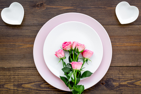 Simple color table setting for celebration with roses, pink plates and heart-shaped saucers on wooden kitchen table background top view.の写真素材