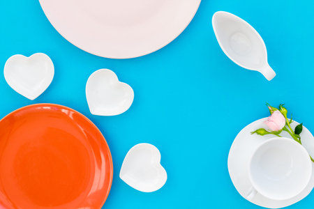 Simple color table setting for celebration with roses, white plates and heart-shaped saucers on blue...