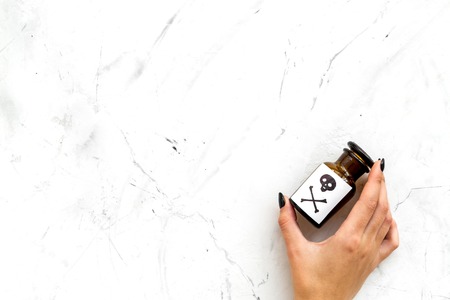 Dangerous addictions, dangerous entertainment. Poison. Female hand hold bottle with skull and crossbones on white stone background top view.の写真素材