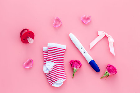 Pregnancy test, socks and hearts on pink background top view
