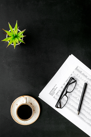 Office desk with pencil, glasses, cup of coffee for lunch on black background top view mockup.の写真素材