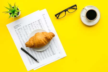 Business lunch with croissant and black coffee on work desk on yellow background top viewの写真素材