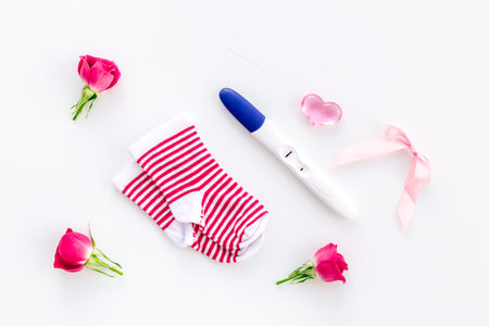 Pregnancy and preparation for childbirth. Babyshower. Pregnancy test near socks and flowers white background top viewの写真素材