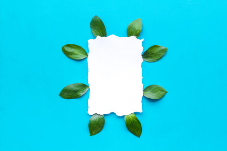 Floral mockup. Leaves around white paper on blue background top view copy space frame