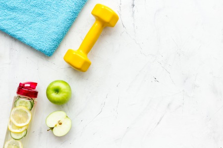 Healthy fruit water for sport, fitness. Bottle of water with lemon and cucumber near sport equipment dumbbells on white stone background top view copy spaceの写真素材