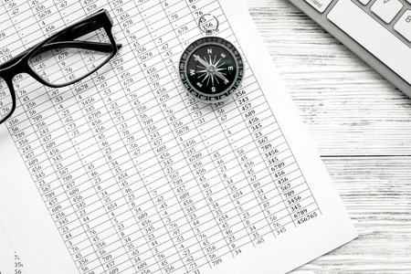 Direction of movement, business direction. Compass, glasses and documents on office workdesk with...