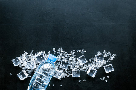 Pile of ice cubes and plastic bottle on black bar table top view mock-upの写真素材
