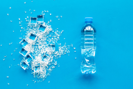 Pile of ice cubes and plastic bottle on blue bar table top view mock-upの写真素材