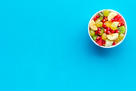 Light healthy breakfast or appetizer. Fruit salad with apple, kiwi and pomegranate in bowl on blue background top view space for textの写真素材