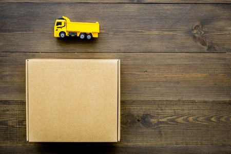 Cargo delivery concept. cardboard box near toy truck on dark wooden background top viewの写真素材