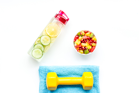 Healthy lifestyle, healthy habits. Detox water, fruit salad, sport equipment dumbbells on white background top viewの写真素材