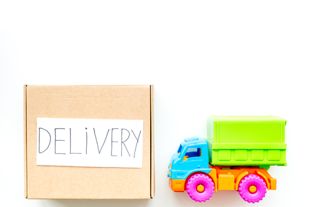 Cargo delivery concept. Cardboard box with written word delivery near toy truck on white background top view.の写真素材
