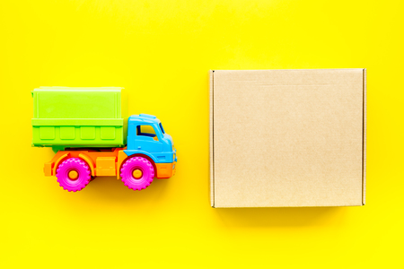 Cargo delivery concept. Cardboard box near toy truck on yellow background top view mockupの写真素材