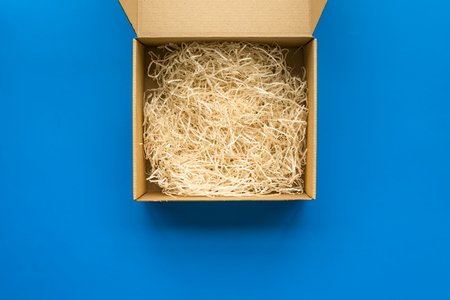E-commerce. Delivery of goods that was purchased online. Empty cardboard box with cut paper on blue background top view.の写真素材