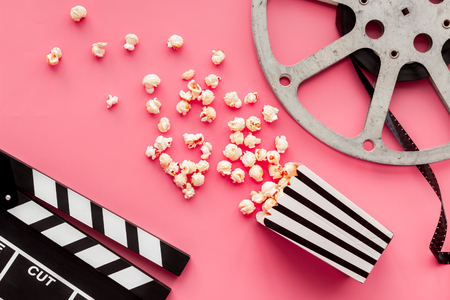 Movie premiere concept. Clapperboard, film stock, popcorn on pink background top view.の写真素材