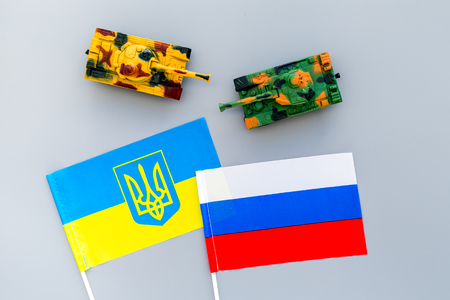 War, confrontation concept. Russia, Ukraine. Tanks toy near Russian and Ukrainian flag on grey background top view.の写真素材