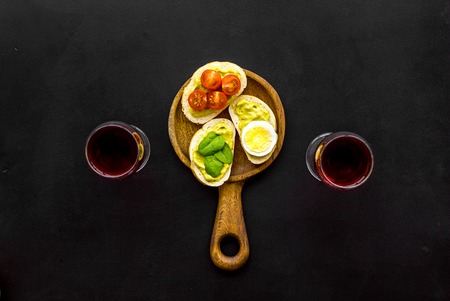 Light appetizer with avocado. Toasts with vegetables and guacamole near glasses of wine on black background top view.の写真素材