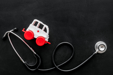 Ambulance service concept. Ambulance vehicle toy near stethoscope on black background top view.の写真素材