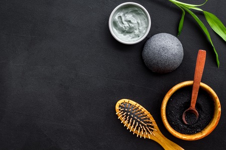 Hair care, hair spa. Cosmetics based on bamboo charcoal powder near comb on black background top view copy spaceの写真素材