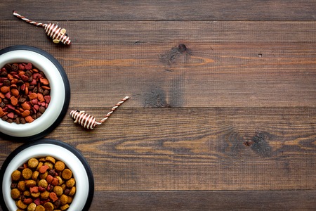 Pets accessories in home. Cat food in bowl, mouse toys on dark wooden background top view copy spaceの写真素材