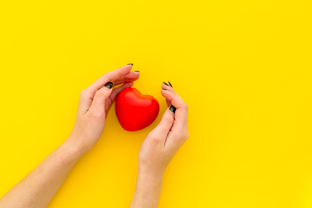Love and relationship. Heart toy in hands as Valentine's day symbol on yellow background top view.の写真素材