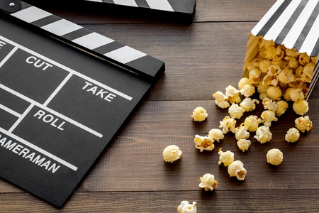 Movie premiere concept. Clapperboard and popcorn on dark wooden background.