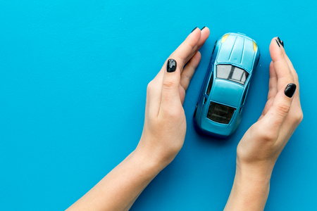 Car insurance concept. Safety of auto. Car toy in female hands on blue background top view copy spaceの写真素材