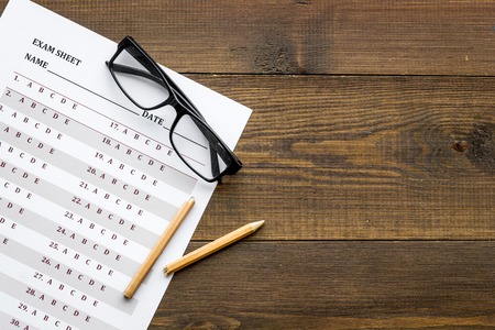 On the exam. Exam sheet, answer near glasses and pencil on dark wooden background top view.の写真素材