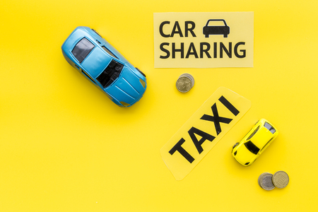 Car sharing vs taxi concept. Comparing car sharing system and taxi. Ship trip concept. Toy cars ans coins on yellow background top view copy spaceの写真素材