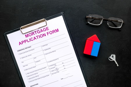 Mortgage concept. Mortgage application form near key and house made of constructor on black...