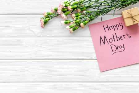 Happy Mothers Day concept. Hand lettering near bouquet of pink carnation and gift box on white wooden background top view space for textの写真素材