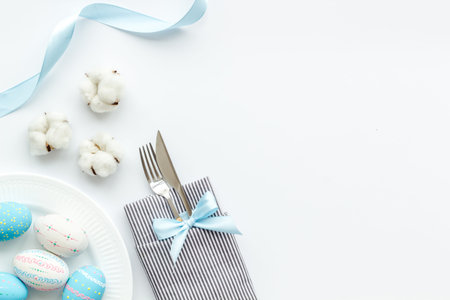 Easter table decoration in blue colors. Plate, cutlery, painted eggs and dry cotton flowers,...