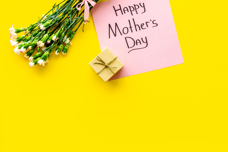 Happy Mother's Day concept. Hand lettering near bouquet of pink carnation and gift box on yellow background top view.の写真素材