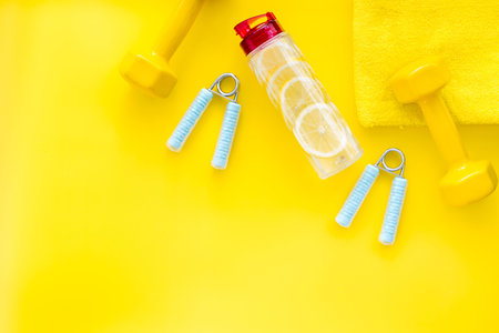 Sport with bars, towel, water and wrist builder on yellow background top view space for text.の写真素材