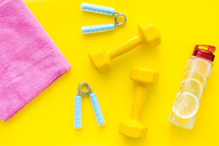 Fitness set with bars, towel, bottle of lemon water and wrist builder on yellow background top viewの写真素材
