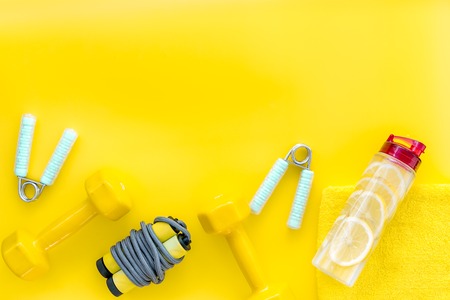 Workout with bars, bottle of water and wrist builder on yellow background top view mockupの写真素材