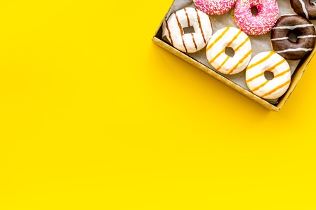 Glazed decorated sweet donuts in box on yellow background flat lay mock upの写真素材