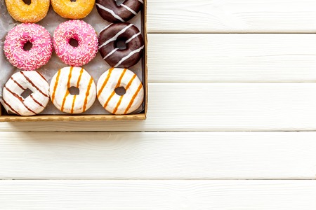 Glazed decorated donuts in box for sweet break on white wooden background flat lay copy space.の写真素材