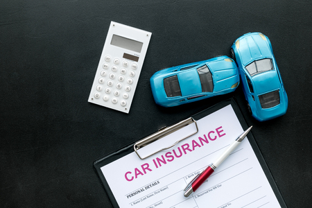 Car insurance concept with form, car toy and calculator on black desk background top viewの写真素材