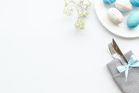 Easter table decoration. Plate, cutlery, painted eggs and dry flower branch on white background top view.の写真素材