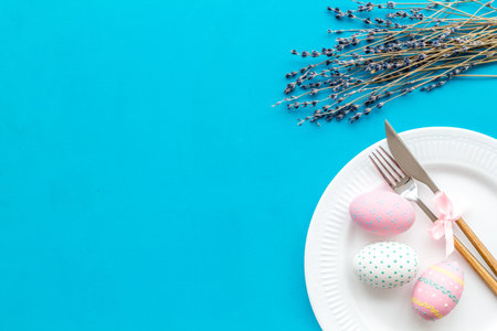Easter dining table in pastel colors. Plate, cutlery, painted eggs, gingerbread and lavender...
