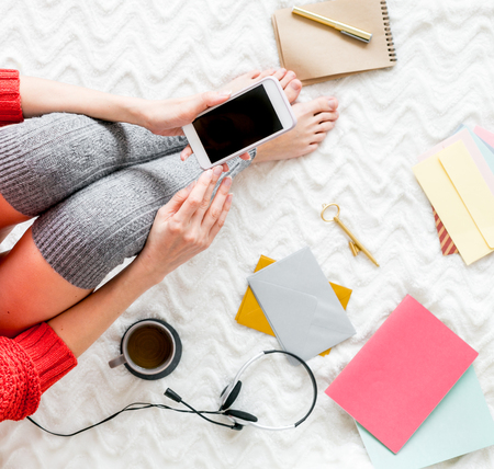 Home office. Girl top view with mobile phone, headphones, cup of tea for breakfast and notebook for work at home concept on bed sheets background.の写真素材
