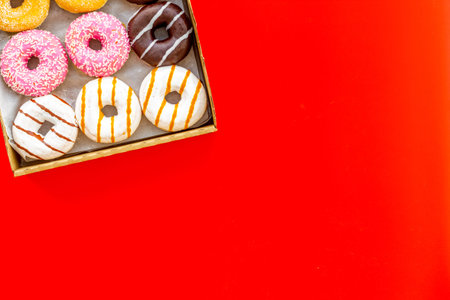 Glazed decorated sweet donuts in box on red background flat lay mock up