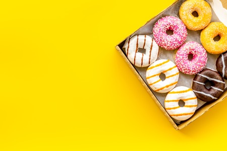Donuts with different flavors in box on yellow background top view mockup.の写真素材