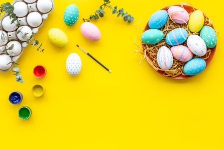 Eggs with colorful paint for Easter tradition on yellow background top view mockupの写真素材