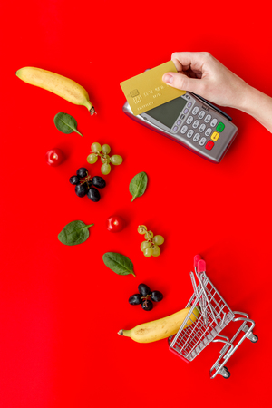 Making purchase products online with card machine, fruits and mini trolley on office desk background top view.の写真素材